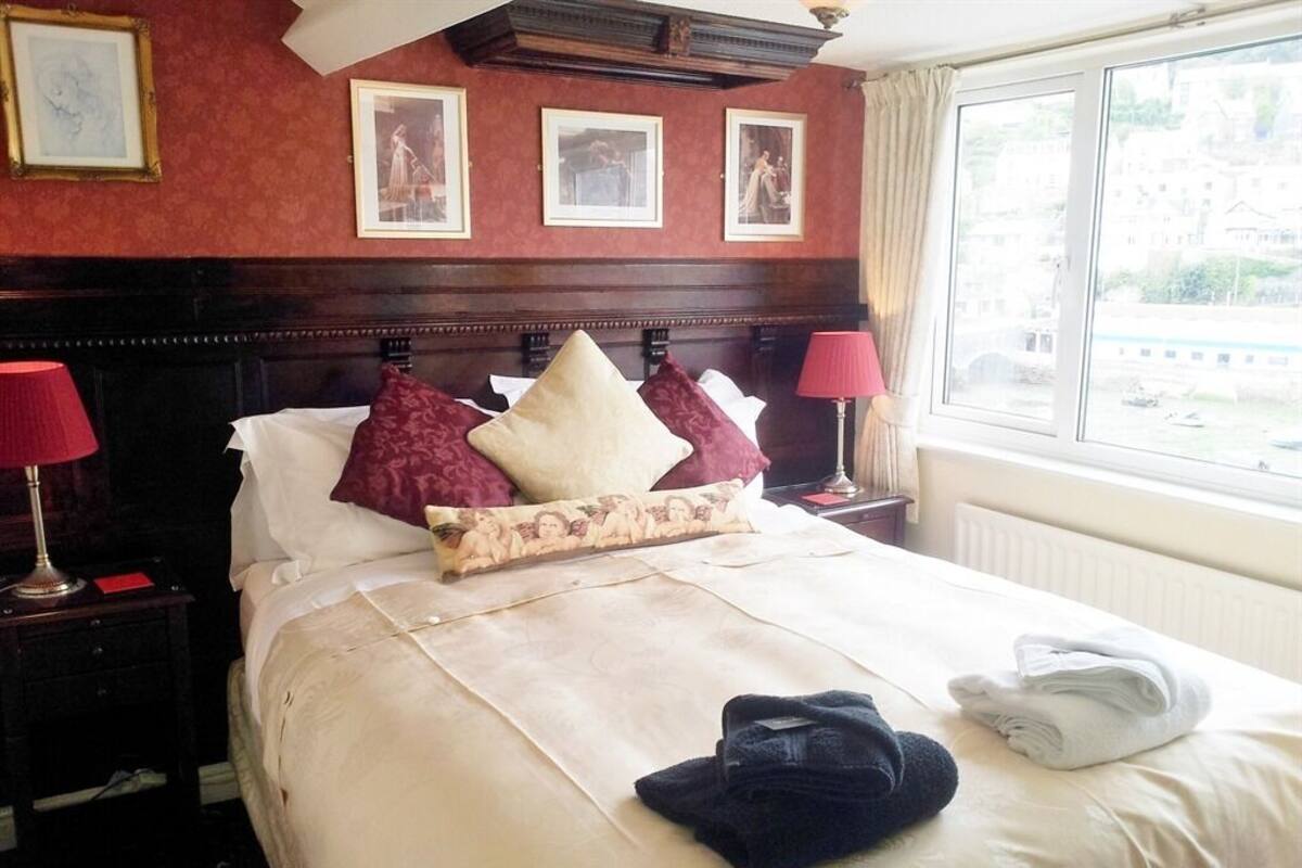 A hotel room with a large bed, two bedside lamps, a window with a view, and framed pictures on the wall.
