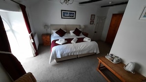 A bedroom with a large bed, a wooden nightstand, a wicker chair, a wooden table with cups and a kettle, and a chandelier. - The White Cottage B&B (Colyton)