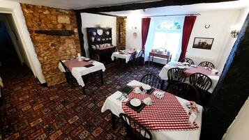 Un comedor con manteles a cuadros, sillas de madera y una pared de piedra. Las mesas están dispuestas con platos, vasos y cubiertos.