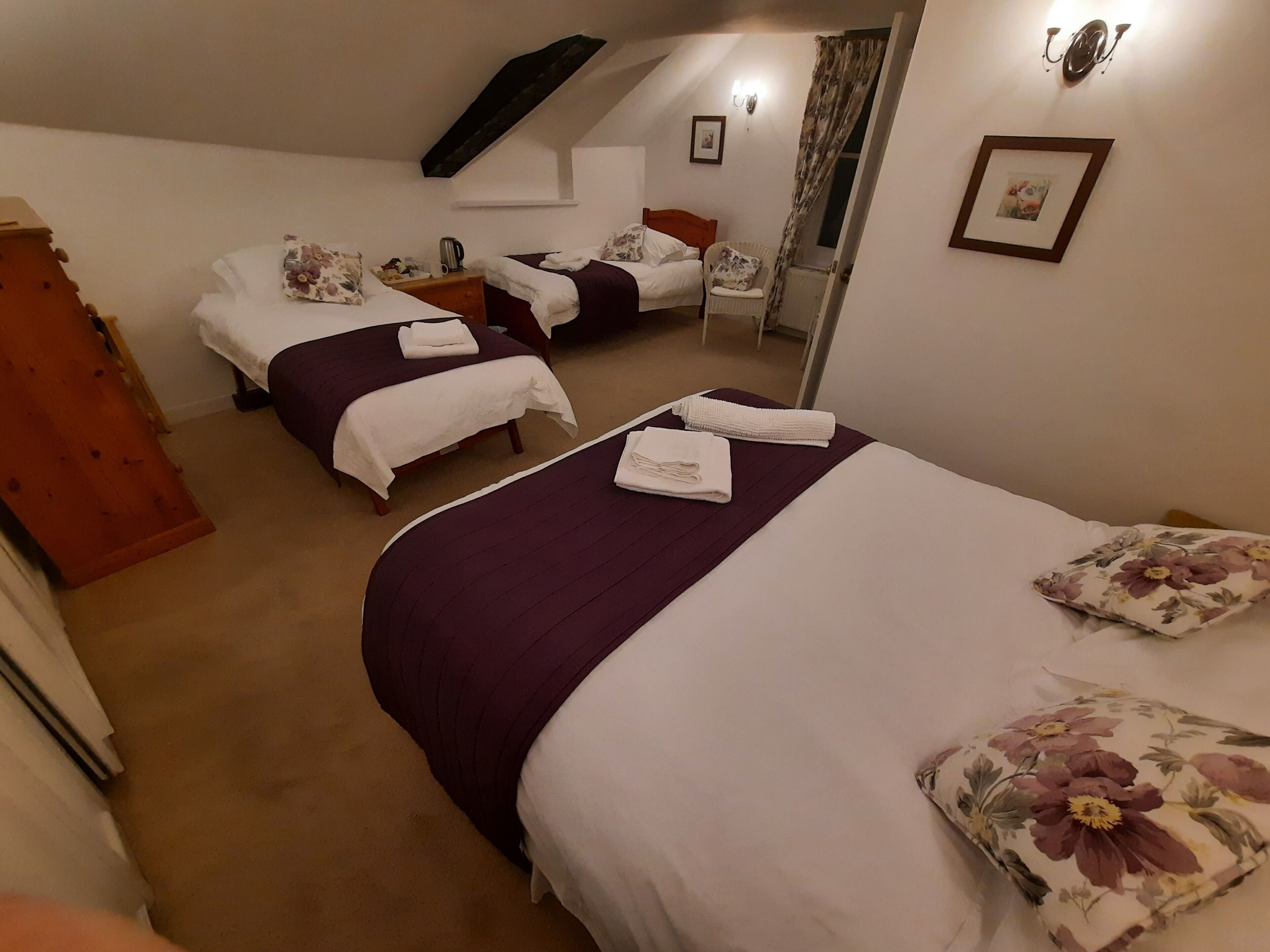 A hotel room with two beds, a wooden wardrobe, a nightstand, a chair, and a small table.