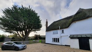 A white house with a thatched roof, a gravel driveway, and a parked car. - The White Cottage B&B (Colyton)