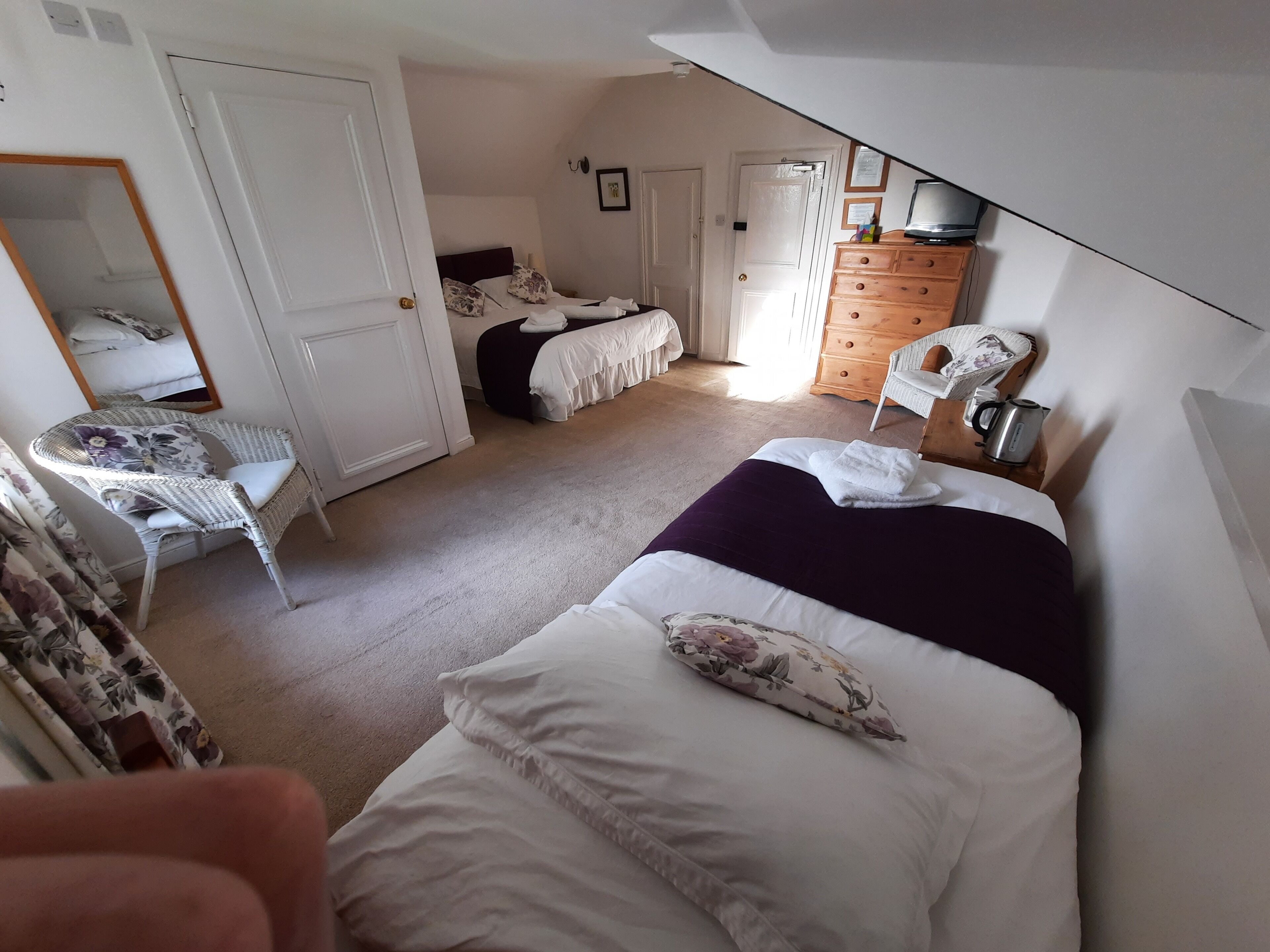 Quarto com duas camas, uma cômoda, uma cadeira e um espelho.