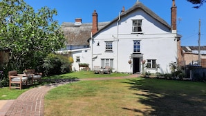 A white building with a brick chimney, a thatched roof, and a paved pathway leading to the entrance. - The White Cottage B&B (Colyton)