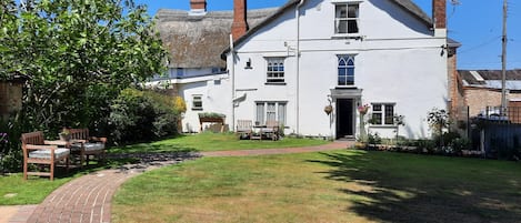 A white building with a brick chimney, a thatched roof, and a paved pathway leading to the entrance.
