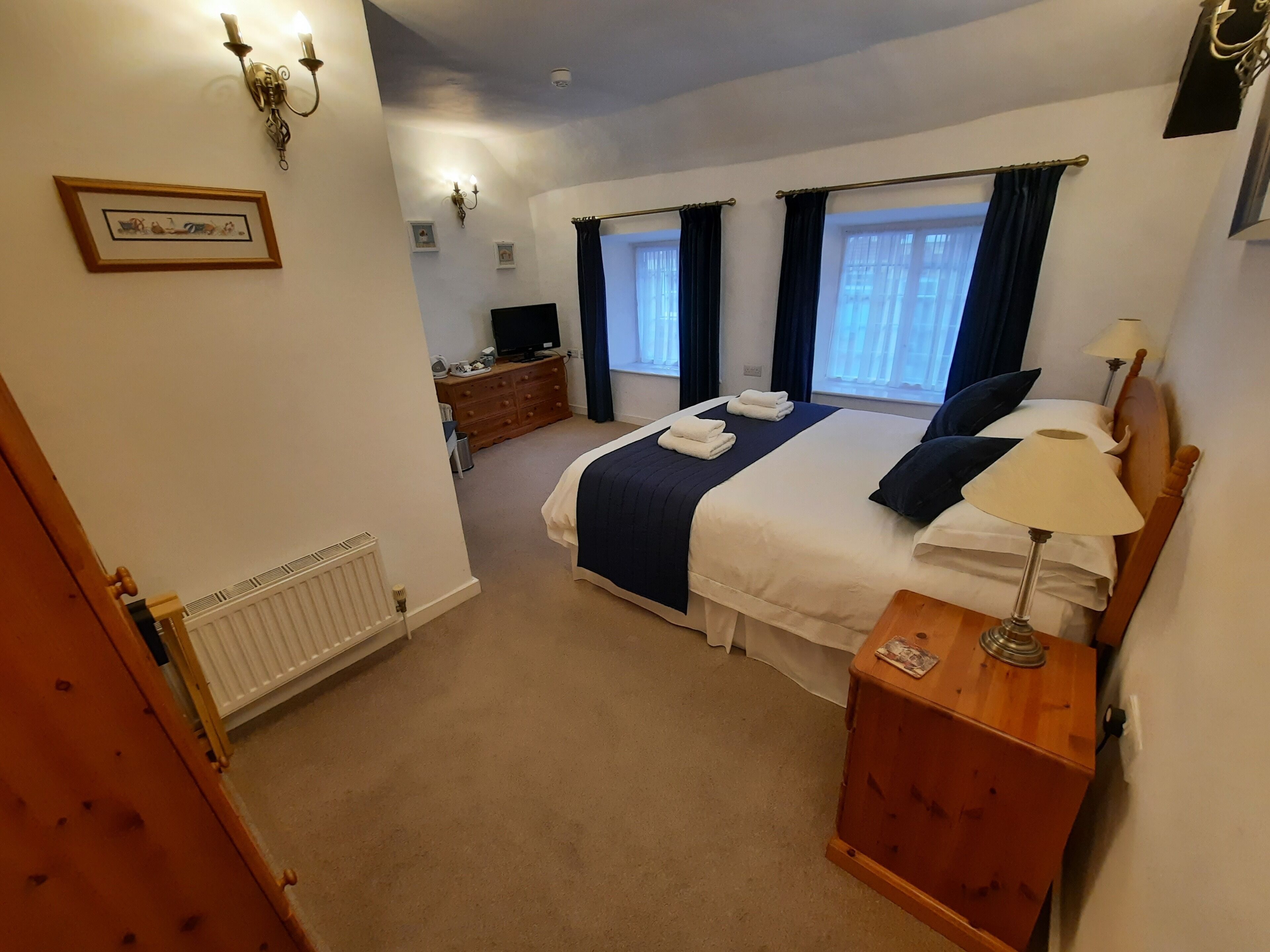 A bedroom with a bed, bedside table, lamp, dresser, and a television.