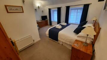 A bedroom with a bed, bedside table, lamp, dresser, and a television.