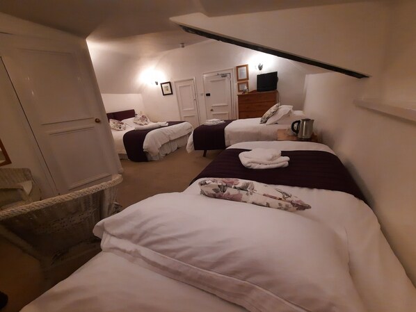 A hotel room with two beds, a wooden dresser, a wicker chair, a white door, and a ceiling light. - The White Cottage B&B (Colyton)