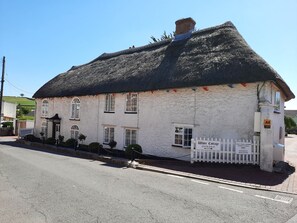 A white building with a thatched roof, a white picket fence, and a sign indicating it is White Cottage. - The White Cottage B&B (Colyton)