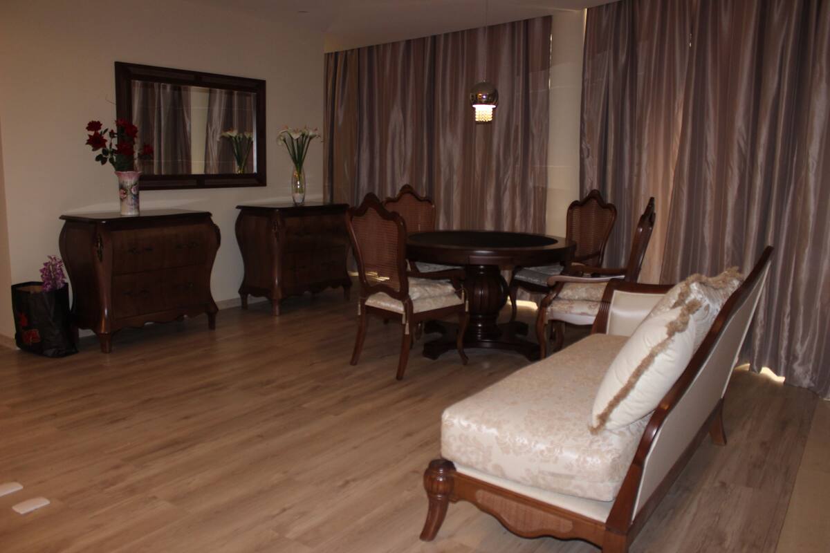 A dining area with a round table, chairs, a sofa, and a cabinet.