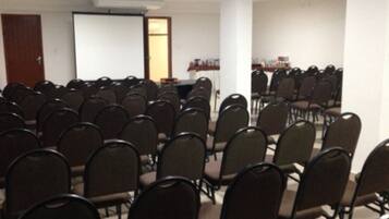 Un salón de conferencias con filas de sillas, una pizarra y una pantalla de proyección.