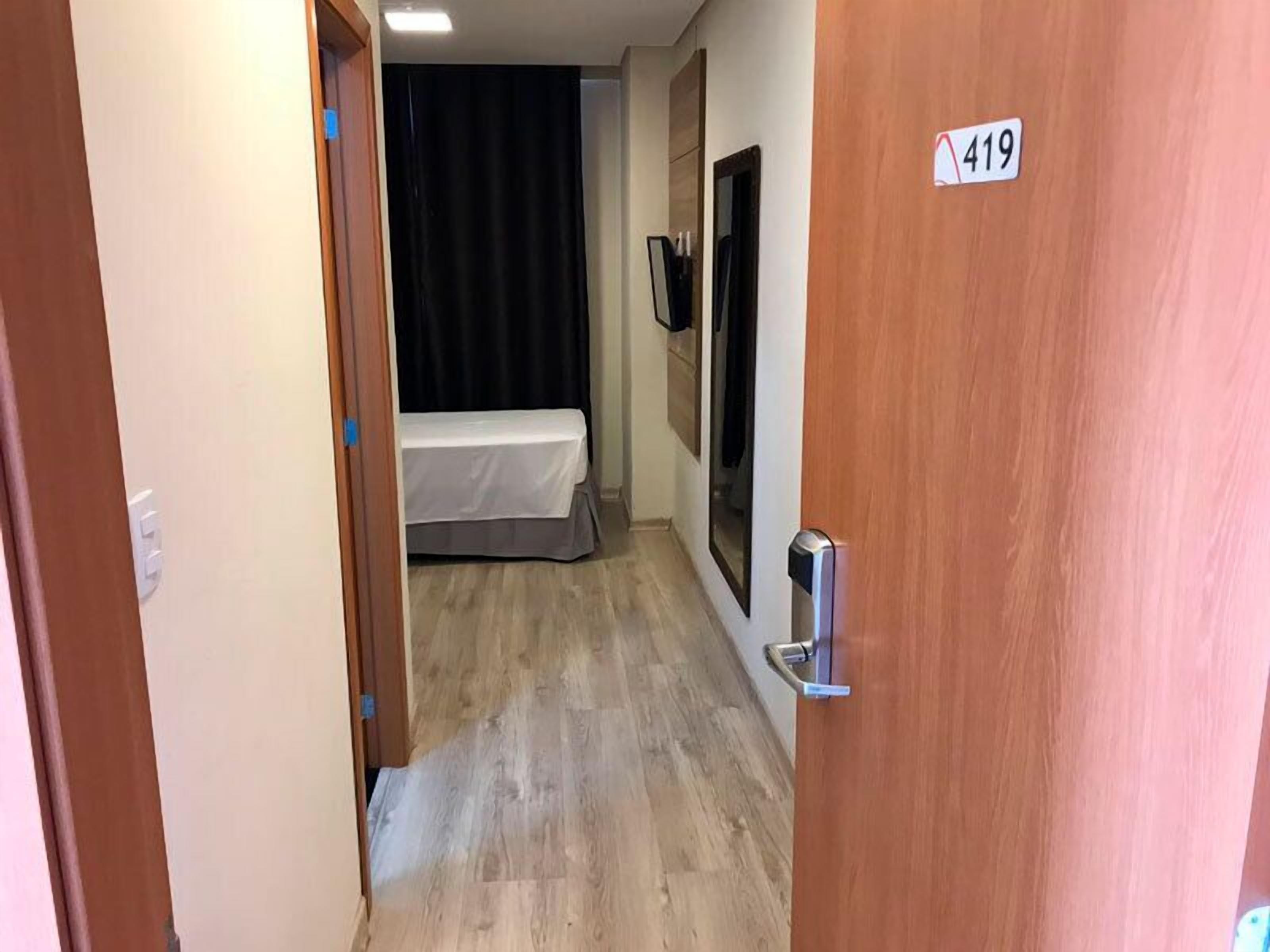 A narrow hallway with a wooden door marked 419, leading to a room with a bed and a black curtain.
