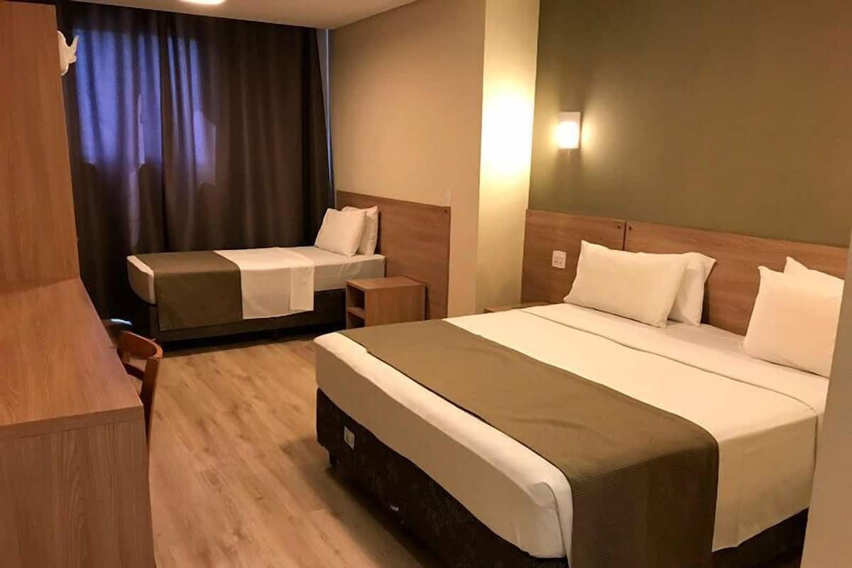 A hotel room with a large bed, a smaller bed, a wooden nightstand, a desk, and a chair.