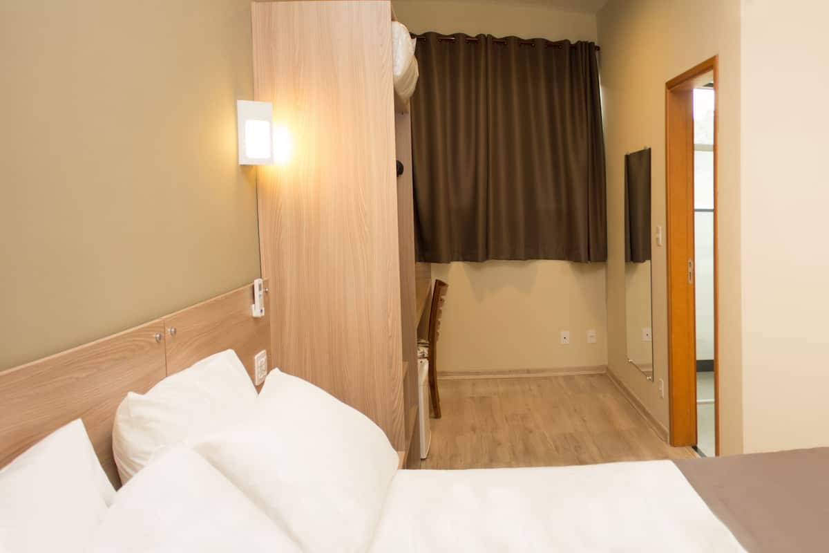 A hotel room with a bed, a TV mounted on the wall, and a door leading to a bathroom.