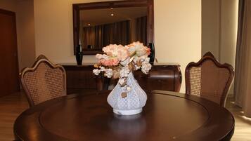 Una mesa redonda de comedor con un jarrón blanco lleno de flores, rodeada por cuatro sillas de madera con respaldo trenzado.