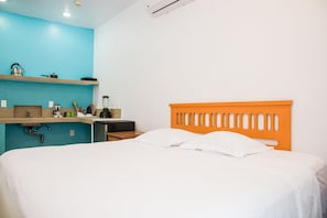 A bedroom with a bed, a nightstand, a shelf with kitchen items, and a window. - Villa Elena Isla Mujeres (Isla Mujeres)