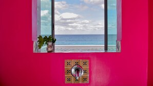Uma janela com vista para o oceano, uma planta em vaso e uma parede revestida com azulejos.
