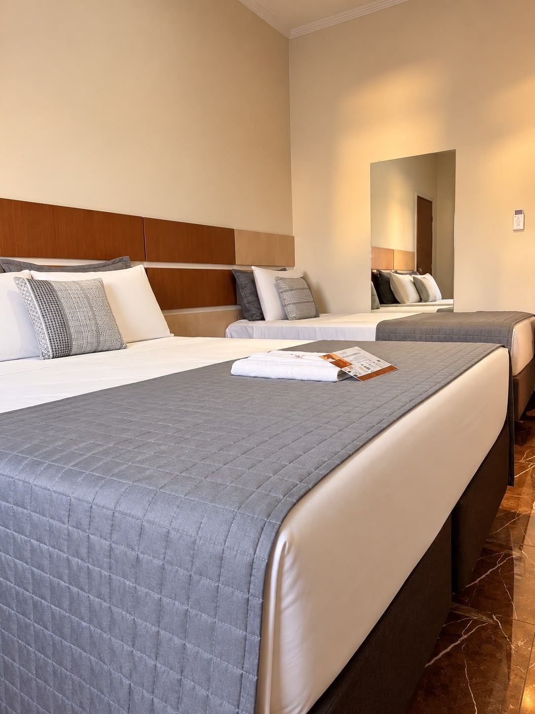 A hotel room with two beds, a wooden headboard, and a mirror on the wall.