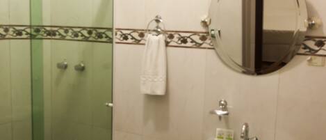 A bathroom with a glass shower enclosure, a pedestal sink, a round mirror, and a toilet.