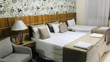 Quarto de hotel com duas camas, um sofá, uma luminária e papel de parede floral.