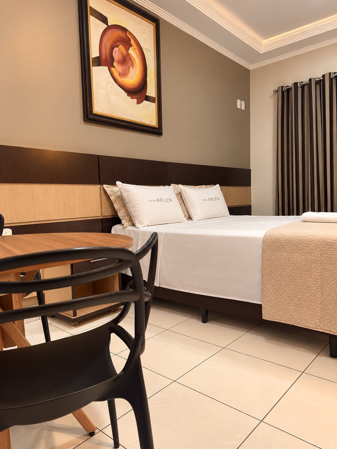 Una camera d'albergo con un letto, una scrivania e una sedia. Sopra il letto, un quadro appeso al muro.