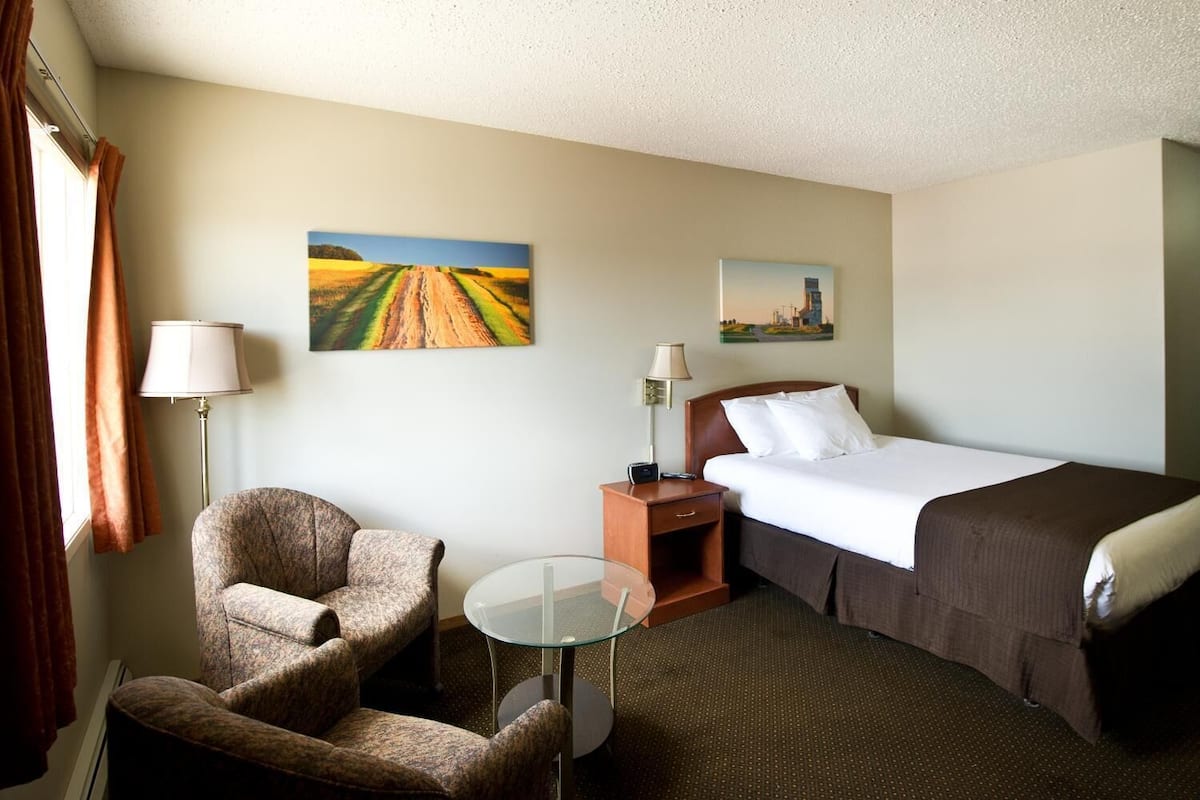 A hotel room with a bed, a chair, a small table, and two lamps.