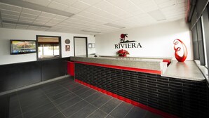 A reception area with a white ceiling, a reception desk with a red accent, a clock, and a logo on the wall.
