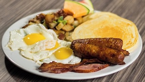 A plate of breakfast food including eggs, bacon, sausages, hash browns, toast, and a slice of melon.