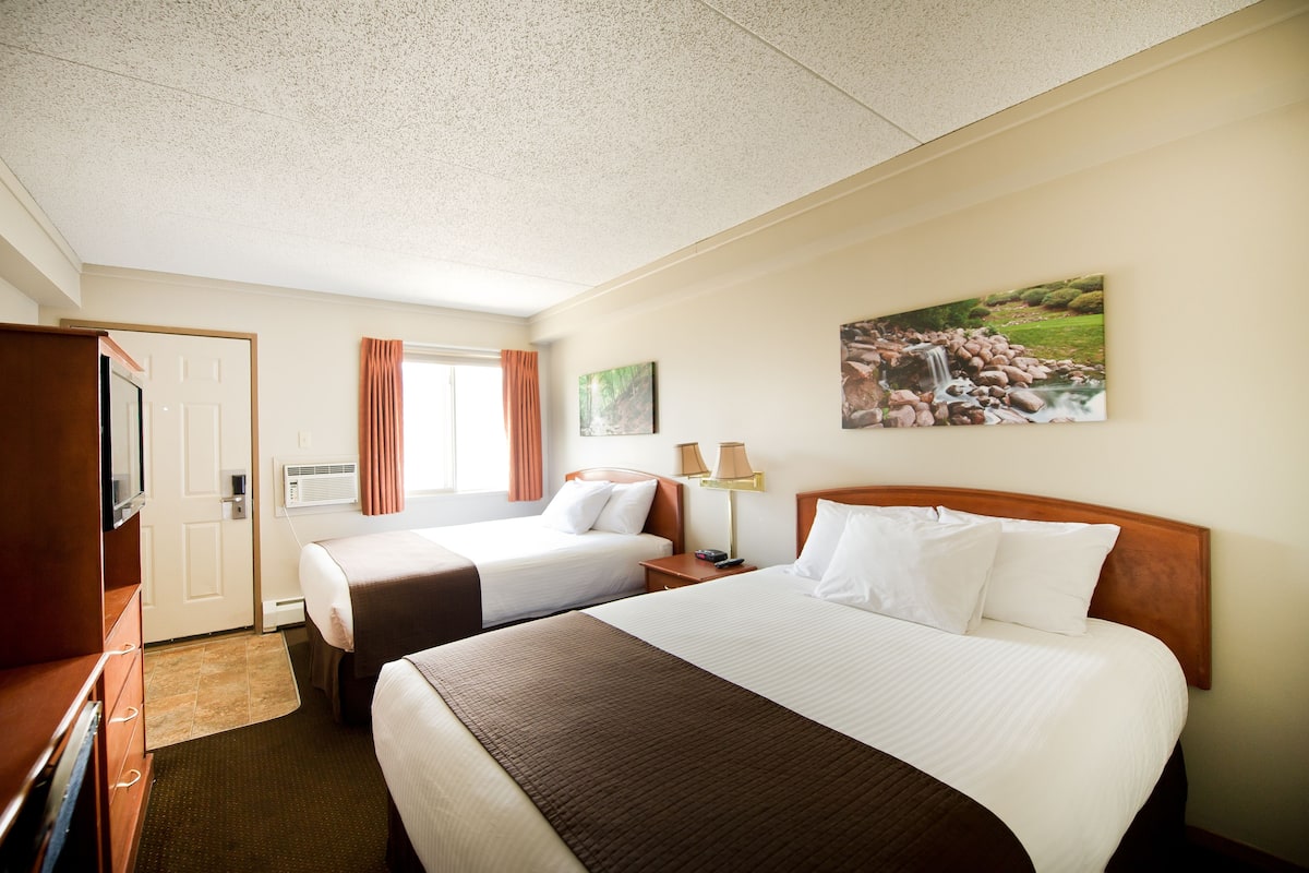 A hotel room with two beds, a television, a desk, and a painting on the wall.