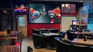 A bar and grill with multiple seating areas, a TV screen displaying hockey games, and a sign indicating it's The Riv bar & grill.