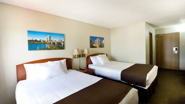 A hotel room with two beds, a nightstand, two lamps, and two paintings on the wall.