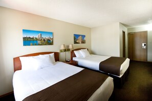 A hotel room with two beds, a nightstand, two lamps, and two paintings on the wall. - Riviera Motor Inn (Saskatoon)