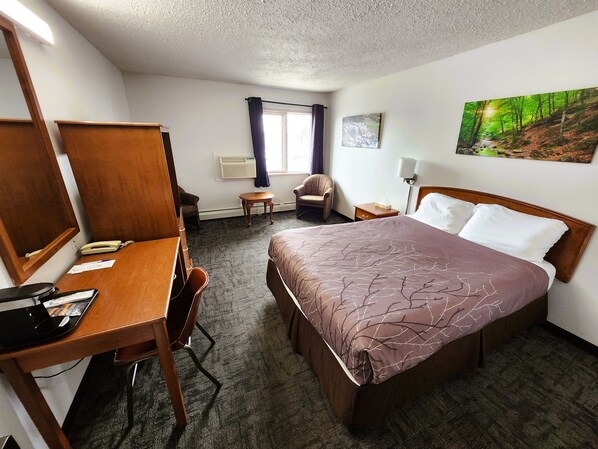 A hotel room with a bed, desk, chair, and a painting on the wall.