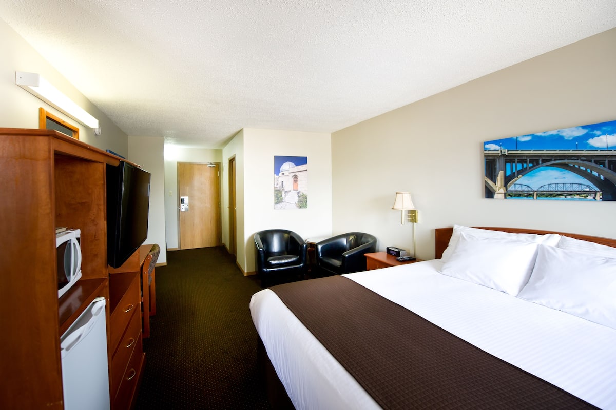 A hotel room with a bed, a television, a desk, a chair, and a microwave.