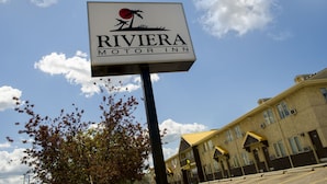 A sign for the Riviera Motor Inn with a clear sky and a building in the background.
