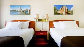 A hotel room with two beds, a nightstand with lamps, and two framed pictures on the wall.