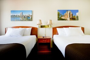 A hotel room with two beds, a nightstand with lamps, and two framed pictures on the wall.