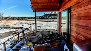 A wooden cabin with a covered porch, a metal table with chairs, and a grill. - Yellowstone River Lodge (Columbus)