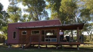 A small, single-story wooden cabin with a porch, surrounded by grass and trees. - Yellowstone River Lodge (Columbus)