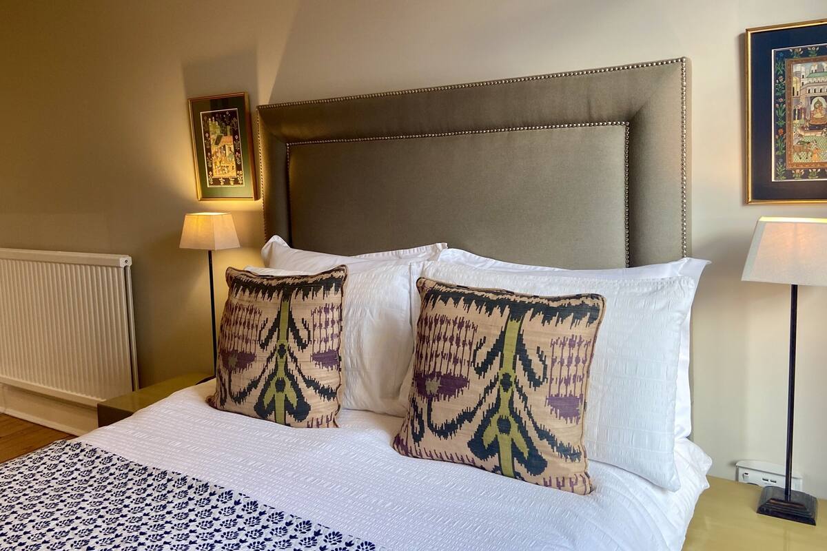 A hotel room with a large bed, two patterned pillows, a headboard, and two wall-mounted lamps.