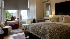Une chambre à coucher avec un grand lit, un bureau, une chaise et une fenêtre donnant sur des immeubles.