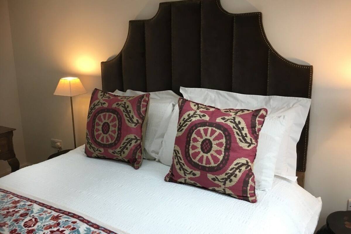 A bed with a dark headboard, two decorative pillows, a white bedspread, and a lamp on a bedside table.