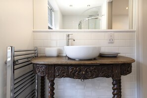 Une salle de bain avec un lavabo sur colonne blanc, un meuble-lavabo en bois et un porte-serviettes.