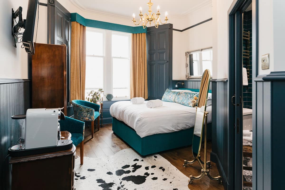 A bedroom with a bed, a chair, a desk, and a mirror.