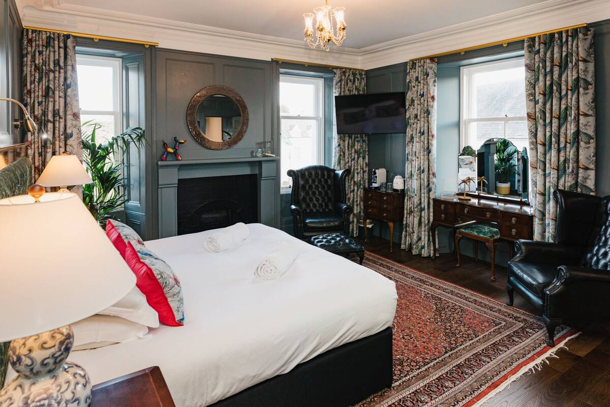 A well-appointed bedroom with a large bed, a fireplace, a television, and a desk with a chair.