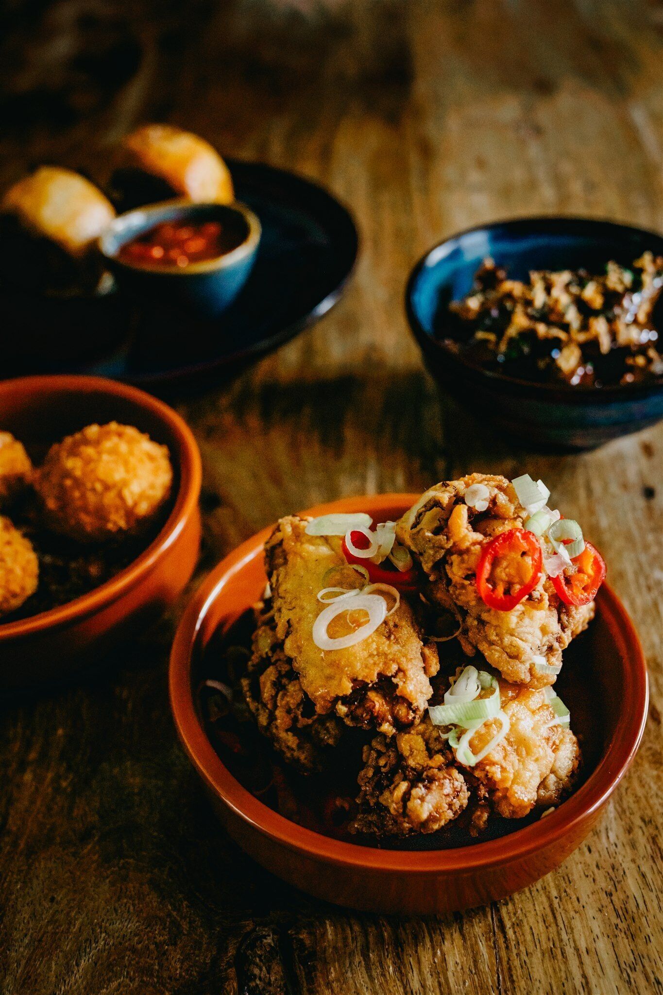 A wooden table with bowls containing fried food and dipping sauces.