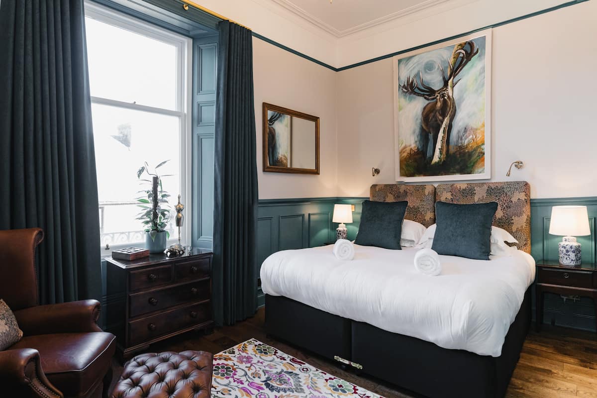 A hotel room with a large bed, a chair, a dresser, a lamp, and a painting on the wall.