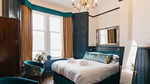 A bedroom with a large bed, a chair, a mirror, and a window with curtains. - Coorie Inn Restaurant and Rooms (Crieff)