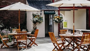An outdoor seating area with wooden tables and chairs, covered by umbrellas, and a small building with a sign reading "Rosemary". - Coorie Inn Restaurant and Rooms (Crieff)