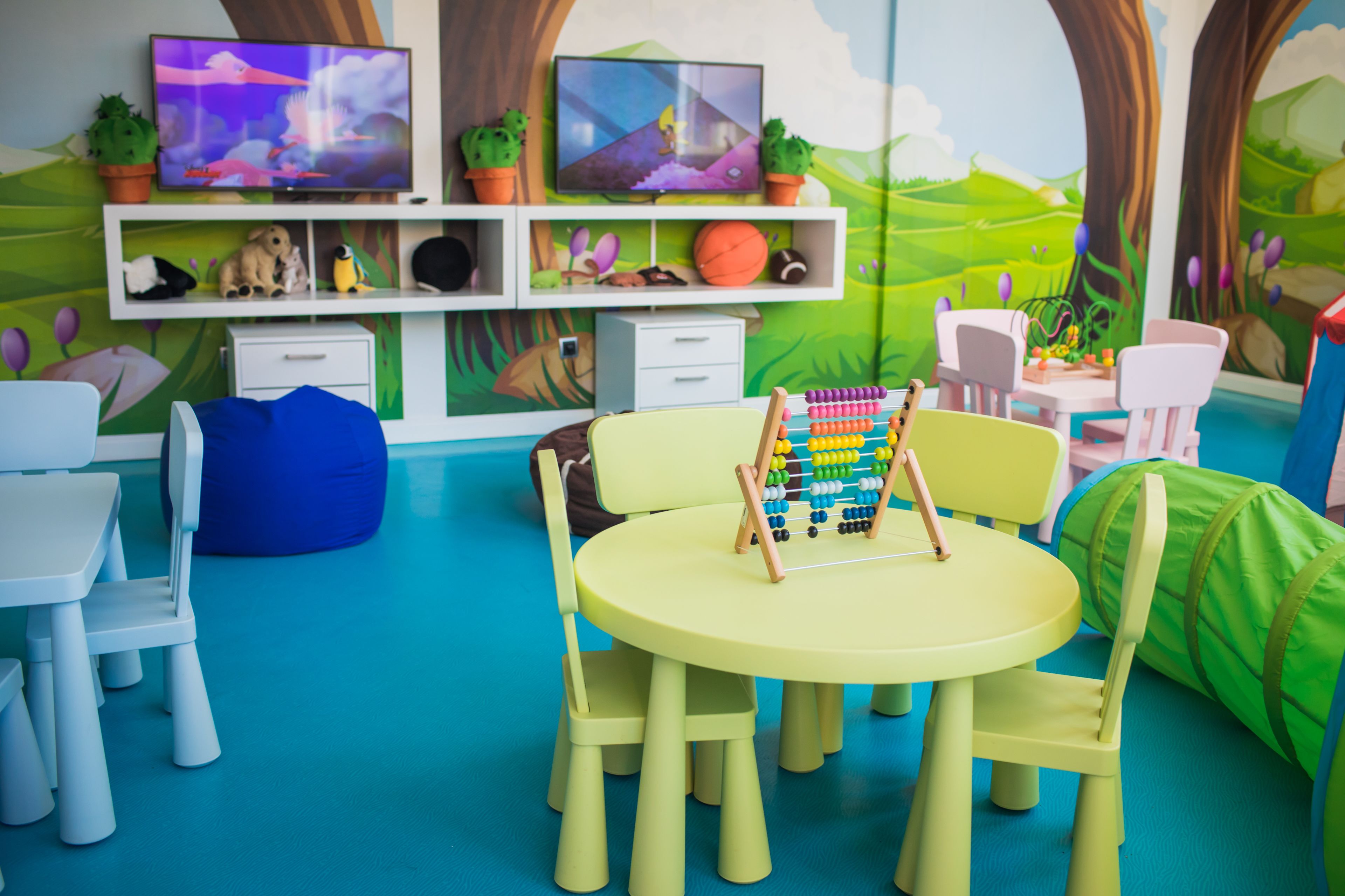 A children's playroom with a round table, chairs, a bean bag, and a TV on a shelf.