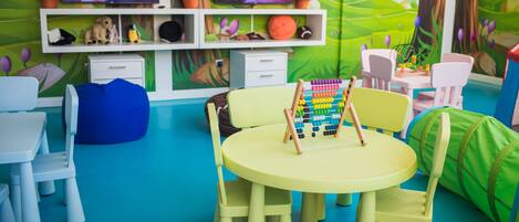 A children's playroom with a round table, chairs, a bean bag, and a TV on a shelf.